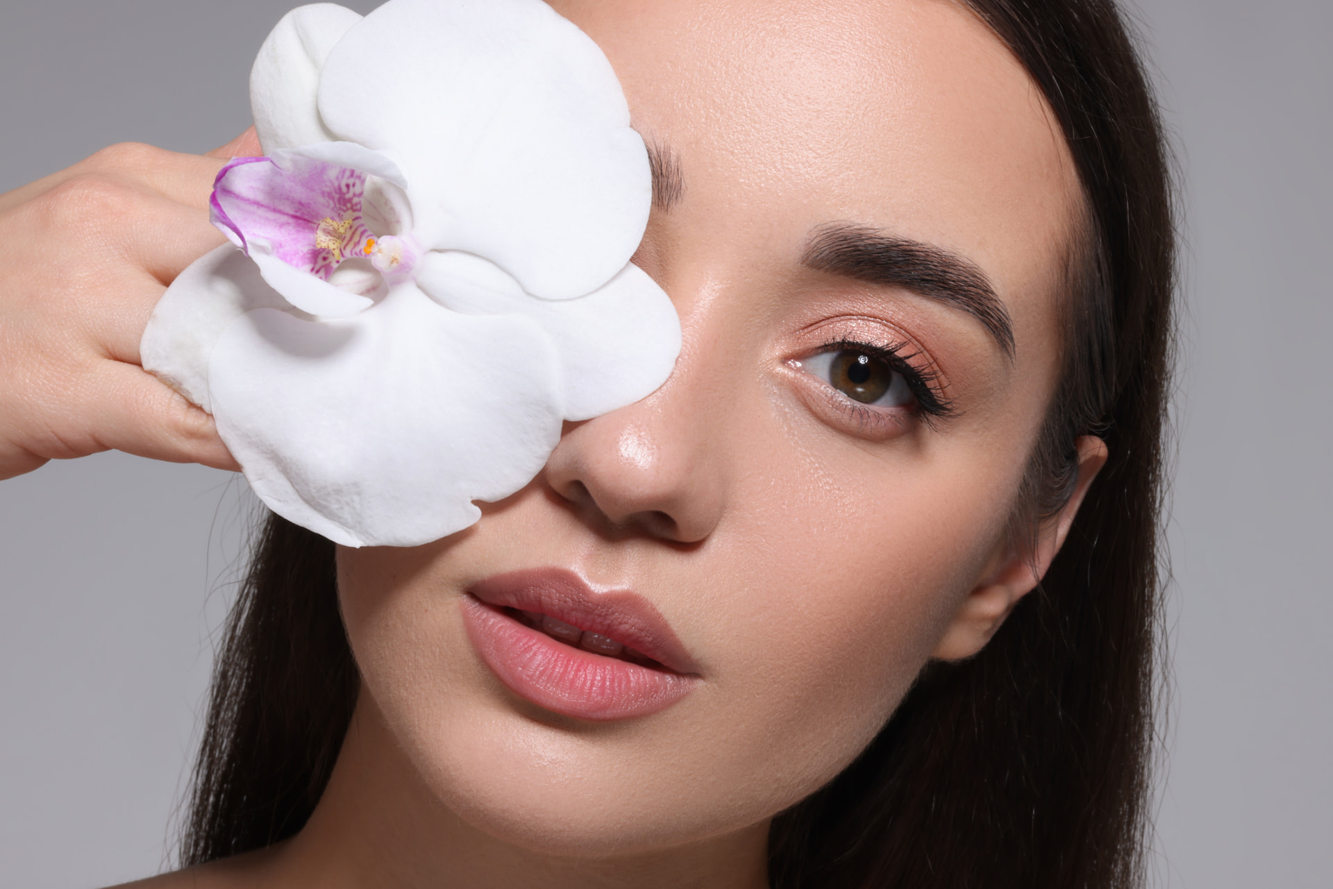 Frau mit weißer Orchideenblüte vor dem Gesicht – Hautpflege mit Ruhe und Präzision